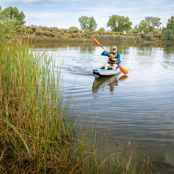 Senior male paddler is paddling an inflatable touring kayak on a calm  lake in Colorado in early fall scenery.