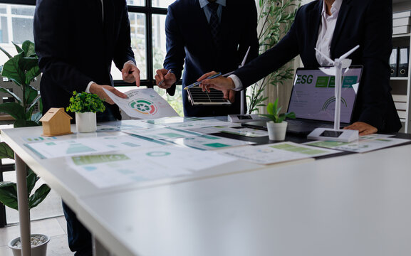 Business team analyzing esg green energy reports, discussing sustainability strategy with wind turbine and solar panel models