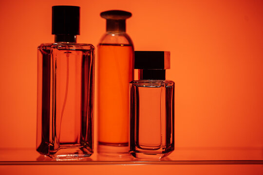 Three elegant glass perfume bottles with black caps displayed on a shelf against a warm orange background, showcasing various shapes and sizes of fragrance containers