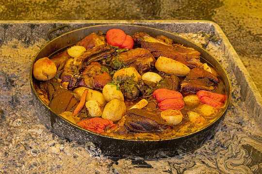 Fresh organic vegetables and pork meat with spices cooked in metal pot and sold outside on market