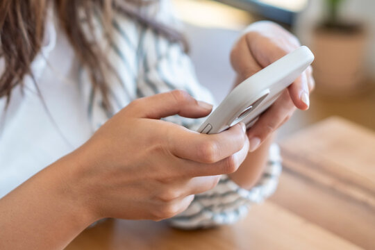 Young woman using smartphone at a wooden table, hands tapping screen while texting and browsing social media in a casual home setting