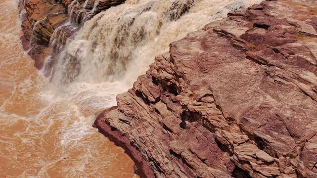 Raging waterfall displaying immense power and fluid dynamics. Slow push in reveals turbulent white water crashing against rocky banks. Perfect for energetic concepts and nature documentaries.