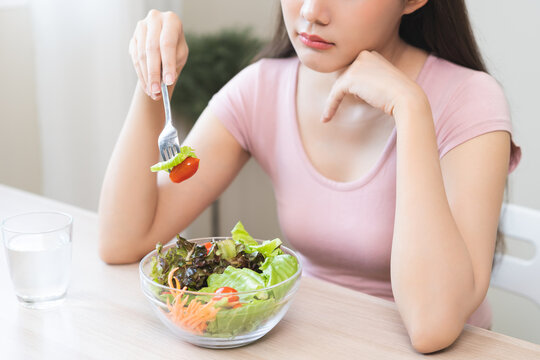 Diet in bored face, unhappy beautiful asian young woman, girl on dieting, holding fork at tomato on salad plate, dislike or tired with eat fresh vegetables. Nutrition of clean, healthy food good taste