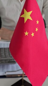 Person sits at a desk while using a calculator next to a Chinese flag during working hours