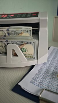 Counting cash with a bill counting machine in an office setting while recording transaction details on a sheet