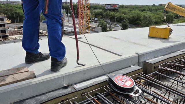 High altitude construction worker standing upright on the roof edge with fall arrest block attached to reinforcement steel structure.