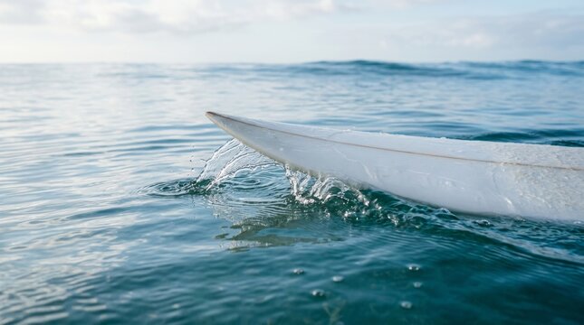A surfboard slices through blue ocean water with spray.