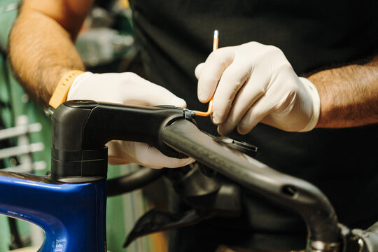 Male bicycle mechanic wearing protective gloves adjusts a road bike handlebar with a hex key. Close-up shows professional bicycle maintenance in a repair workshop
