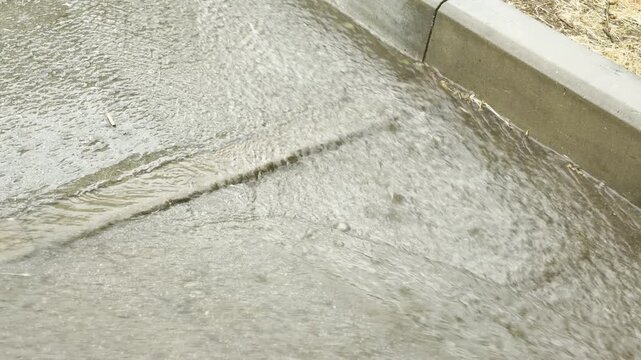Rainwater flows rapidly down a concrete curb along an asphalt road. A lone leaf floats softly in the rushing current. The moody stream brings a calm feeling of quiet refreshment.