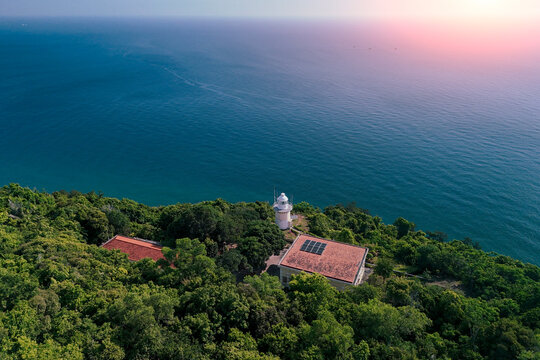 Lighthouse surrounded by dense jungle vegetation sits on the rocky coast of Son Tra Peninsula in Danang Vietnam under the soft golden light of sunset