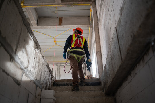 Construction Worker Wearing Safety Harness and Helmet on Stairway at Building Site