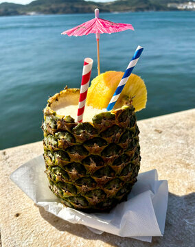 Tropical Pineapple Cocktail by the Sea with Colorful Straws and Beach Umbrella