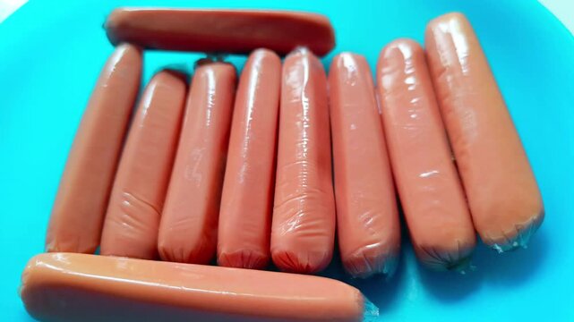 Packaged raw frankfurter sausages arranged on bright blue surface close up