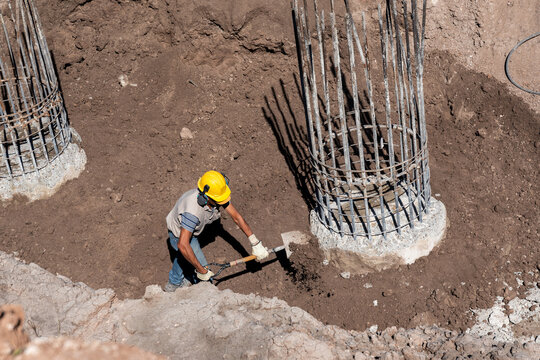 Construction worker shoveling dirt near concrete pile rebar cage in foundation pit