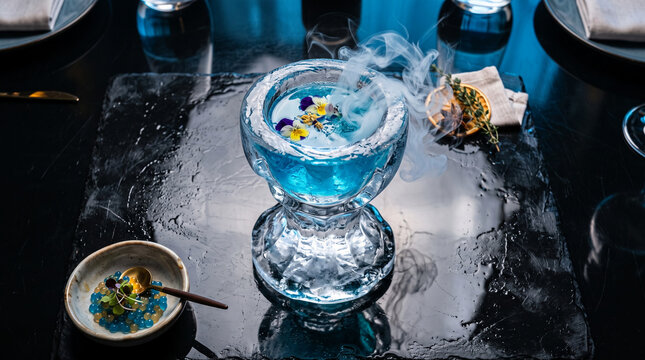 Elaborate blue cocktail with smoke and edible flowers on slate