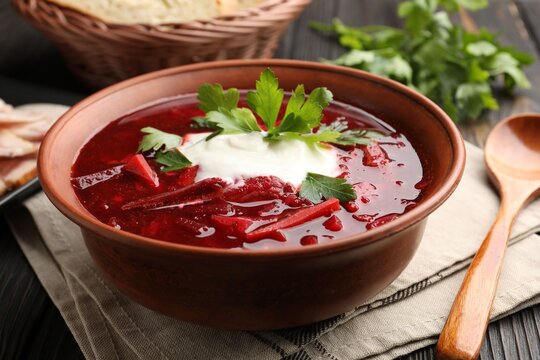 Delicious borscht with sour cream and parsley in bowl on wooden table, closeup