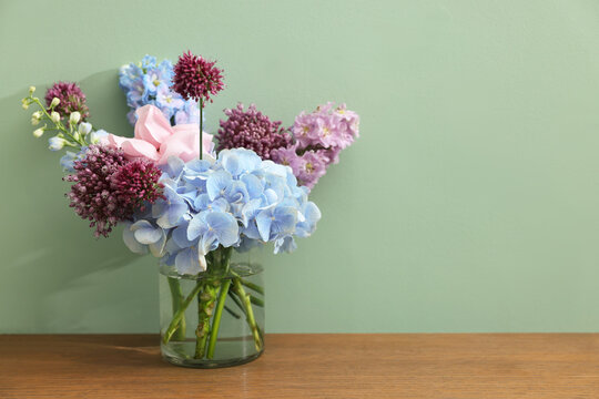 Bouquet of beautiful flowers in vase on wooden table near green wall indoors, space for text