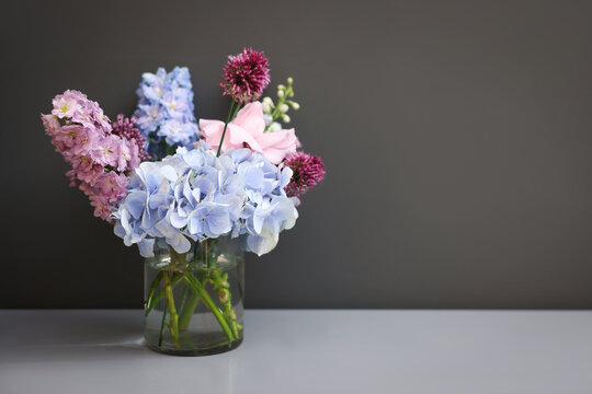 Bouquet of beautiful flowers in vase on white table near grey wall indoors, space for text