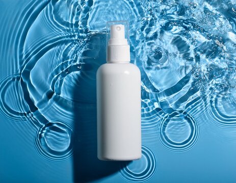 white cosmetic spray bottle with water ripples on a blue background