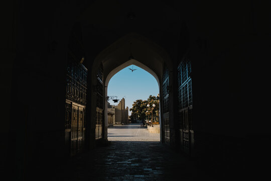 Dark archway framing a view of a sunlit plaza in Bukhara.