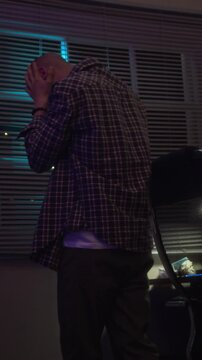 Vertical video of stressed young adult Caucasian man holding head in hands and sitting down in despair near computer screen. Clip is perfect for mental health and gaming addiction campaigns