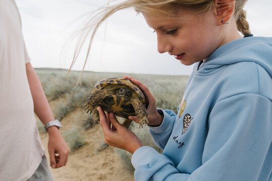 Girl holding a wild tortoise in a dry landscape.