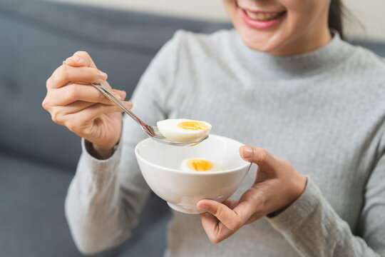 Protein in food, happy smiling asian young woman, girl in diet holding boiled egg, eat with spoon for breakfast in the morning at home. Health care, loss weight people concept.