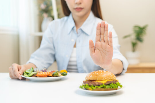 Diet concept, asian young woman hand reject eat burger, hamburger on plate, push out or deny to eat fast, junk food choose green vegetable salad, girl eat low fat for good healthy, getting weight loss
