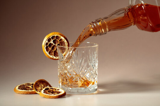Whiskey is poured into a in crystal glass garnished with dried orange slices.