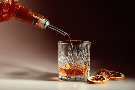 Whiskey is poured into a in crystal glass garnished with dried orange slices.