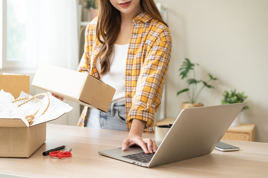 Online sell store, startup small business entrepreneur asian young woman using laptop computer checking purchase product order from web, owner working at home office, prepare pack parcel for delivery.