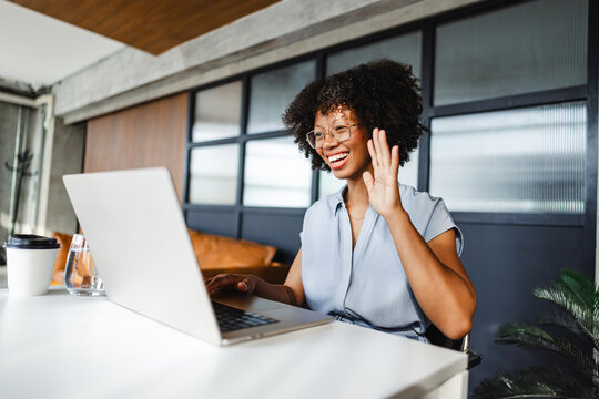 Woman Smiles and Waves While Using Laptop in Home Office