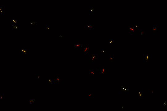 Glowing ember sparks floating in the dark night, small bright orange and yellow particles drifting upwards against a solid black background