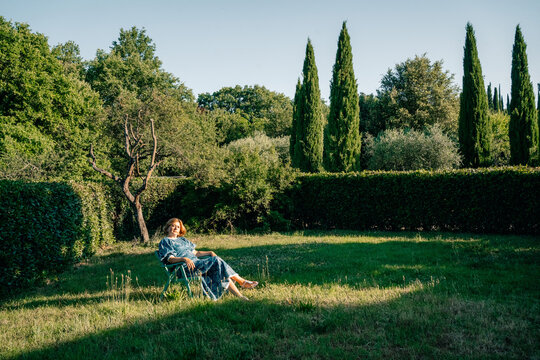Woman Sitting in Garden Under Trees During Bright Daylight
