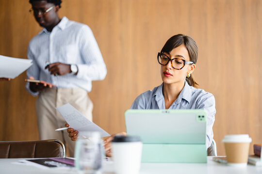 People Work in an Office Setting With Papers and Devices Present