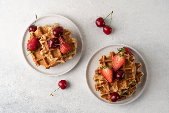 Fresh Belgian cottage cheese waffles served with strawberries and sweet cherries on a light table, top view. High protein breakfast or brunch concept 