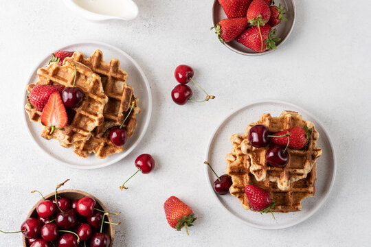 Fresh Belgian cottage cheese waffles served with strawberries and sweet cherries on a light table, top view. High protein breakfast or brunch concept featuring homemade waffles