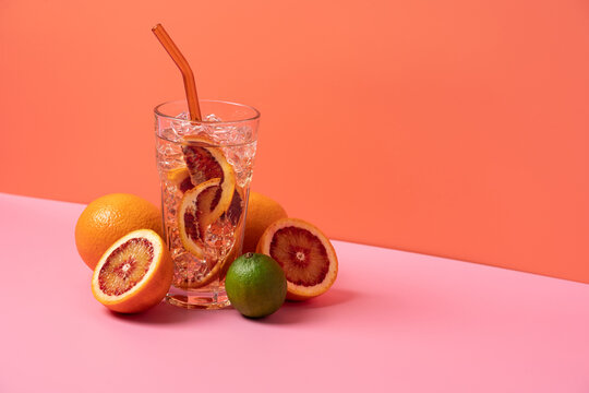 Soda with ice and red orange in clear glass on trendy pink and orange background, minimal aesthetic with copy space, refreshing citrus drink