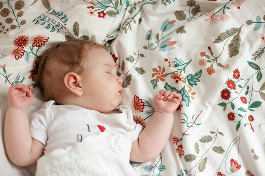 A baby sleeps on a floral patterned sheet