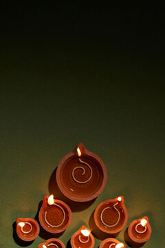 Clay diyas with burning flames arranged on a dark green surface