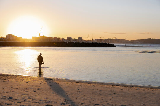 Man stands alone in the water at Currumbin Beach with the sun setting