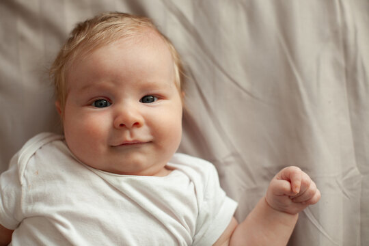 A baby smiles up from soft grey linen bedding