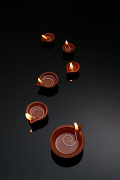 Clay diyas with flickering flames illuminate a dark background