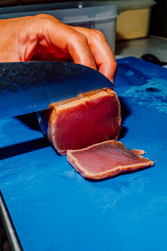 Chef hands slicing seared tuna tataki on a blue cutting board
