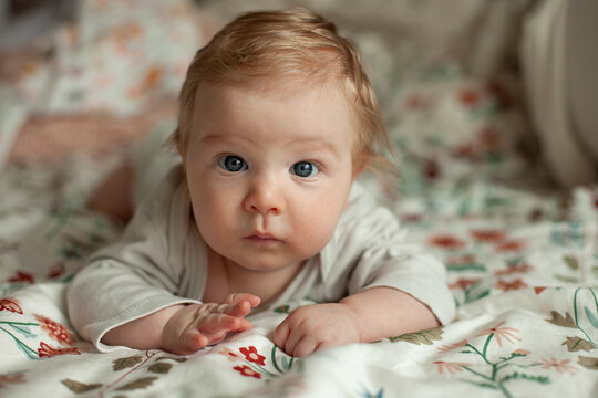 A baby does tummy time on a floral patterned bedsheet