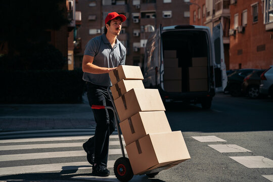Delivery man pushing packages on hand truck in city