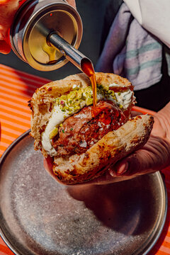 Chef pouring spicy chili oil onto a gourmet meat kofte pita