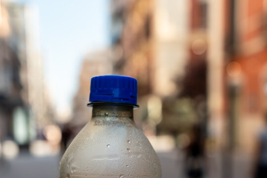 Close up of a condensation covered plastic bottle with blue cap against a blurred city street background
