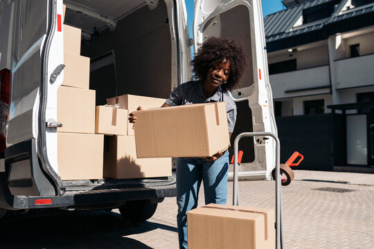 Woman delivery worker unloading cardboard boxes from van