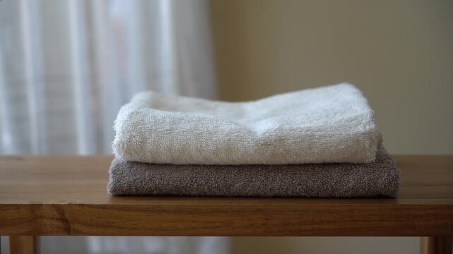Close-up video of neatly stacked textured cotton terry towels placed on a wooden bench. Soft natural textiles with visible fibers and warm cozy aesthetic in a minimalist home environment